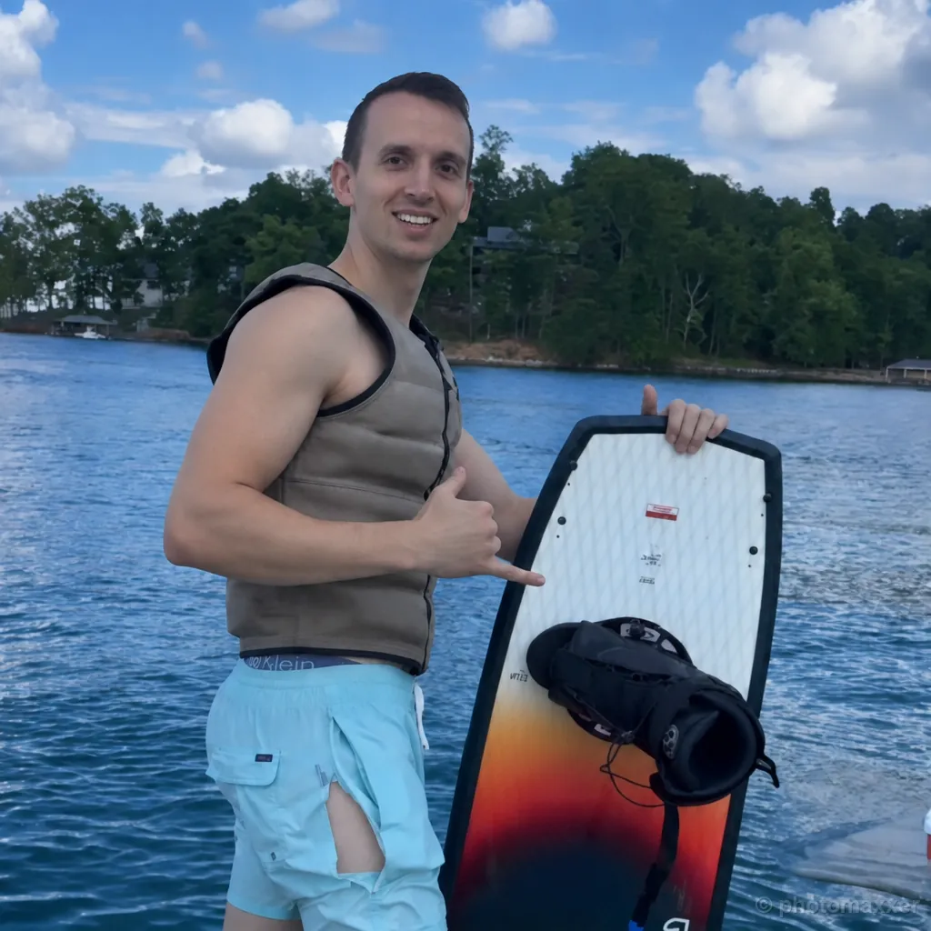 AI-generated Photomaxxer example of a man wearing a life vest and holding a wakeboard beside a lake.